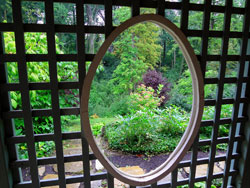 An oval window provides a sneak preview of this expansive woodland garden.
