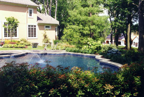 A swimming pool and spa in trefoil shape nested into a wood-side garden.